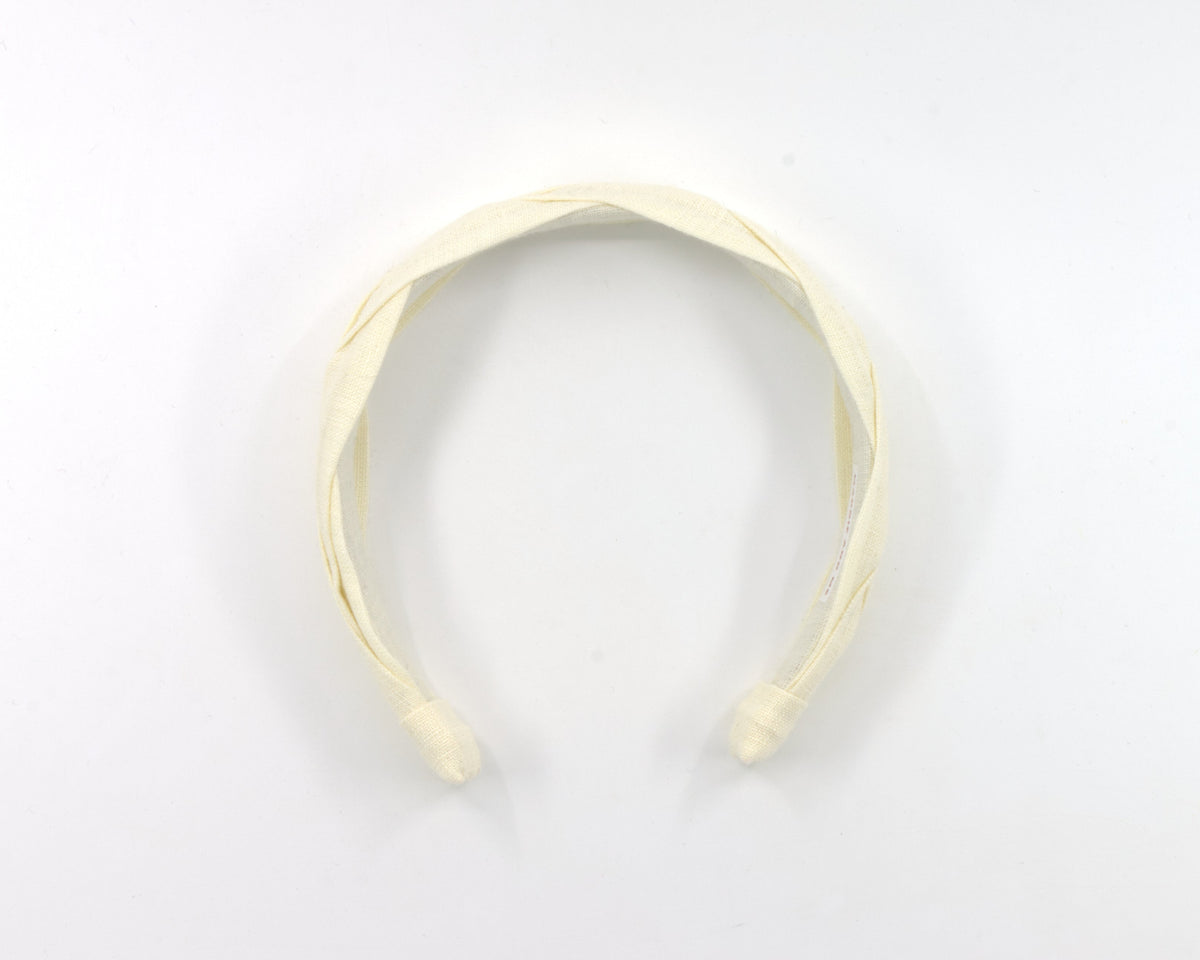 A cream-colored fabric headband with a twisted, braided design, photographed on a plain white background.