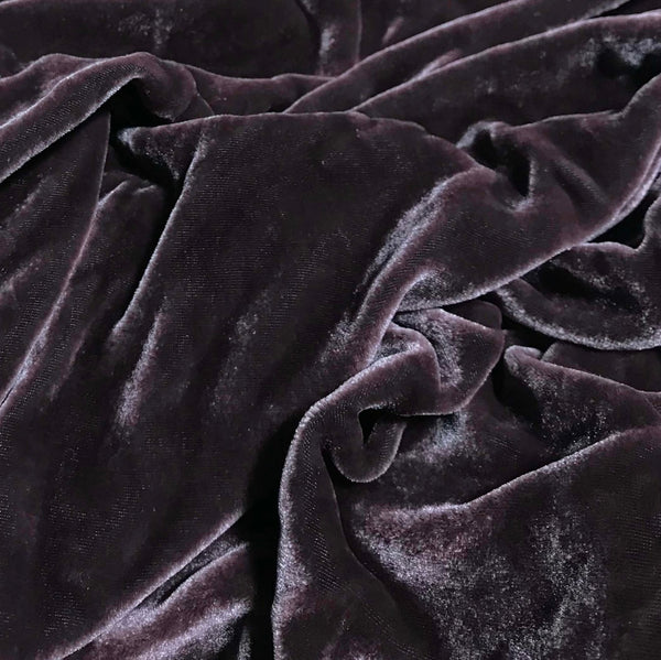A close-up of draped dark mauve velvet fabric, showing its soft texture and rich folds.