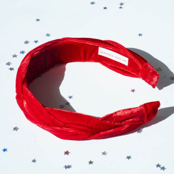 A red braided velvet headband on a white background with star confetti scattered around.