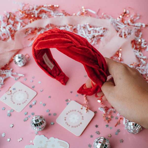 A red braided velvet headband on a pink background with confetti scattered around.