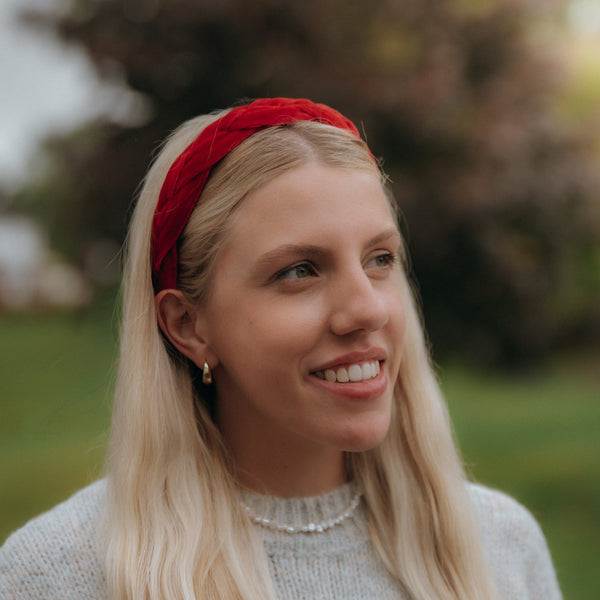Woman with long blonde hair wearing a red headband, smiling outdoors.
