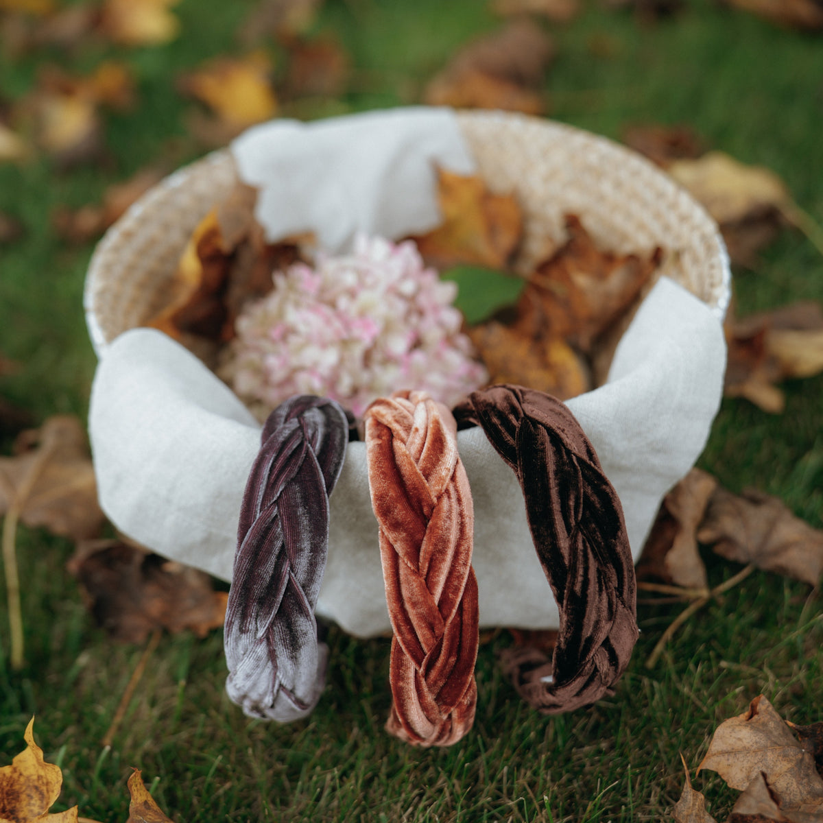Three velvet headbands in a basket on a grassy background with leaves.