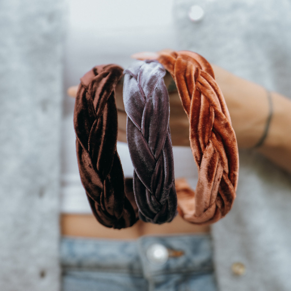 Three velvet braided hairbands in chocolate brown, vintage mauve and copper held by a person wearing a gray sweater. 