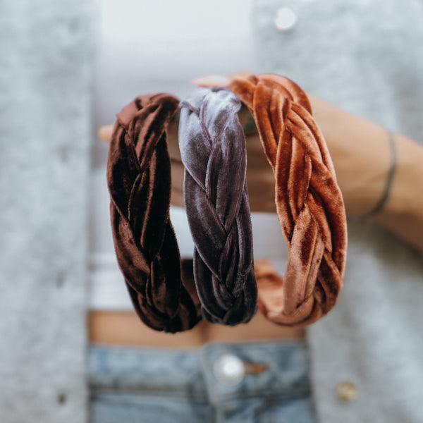 Three velvet braided hairbands in chocolate brown, vintage mauve and copper held by a person wearing a gray sweater. 