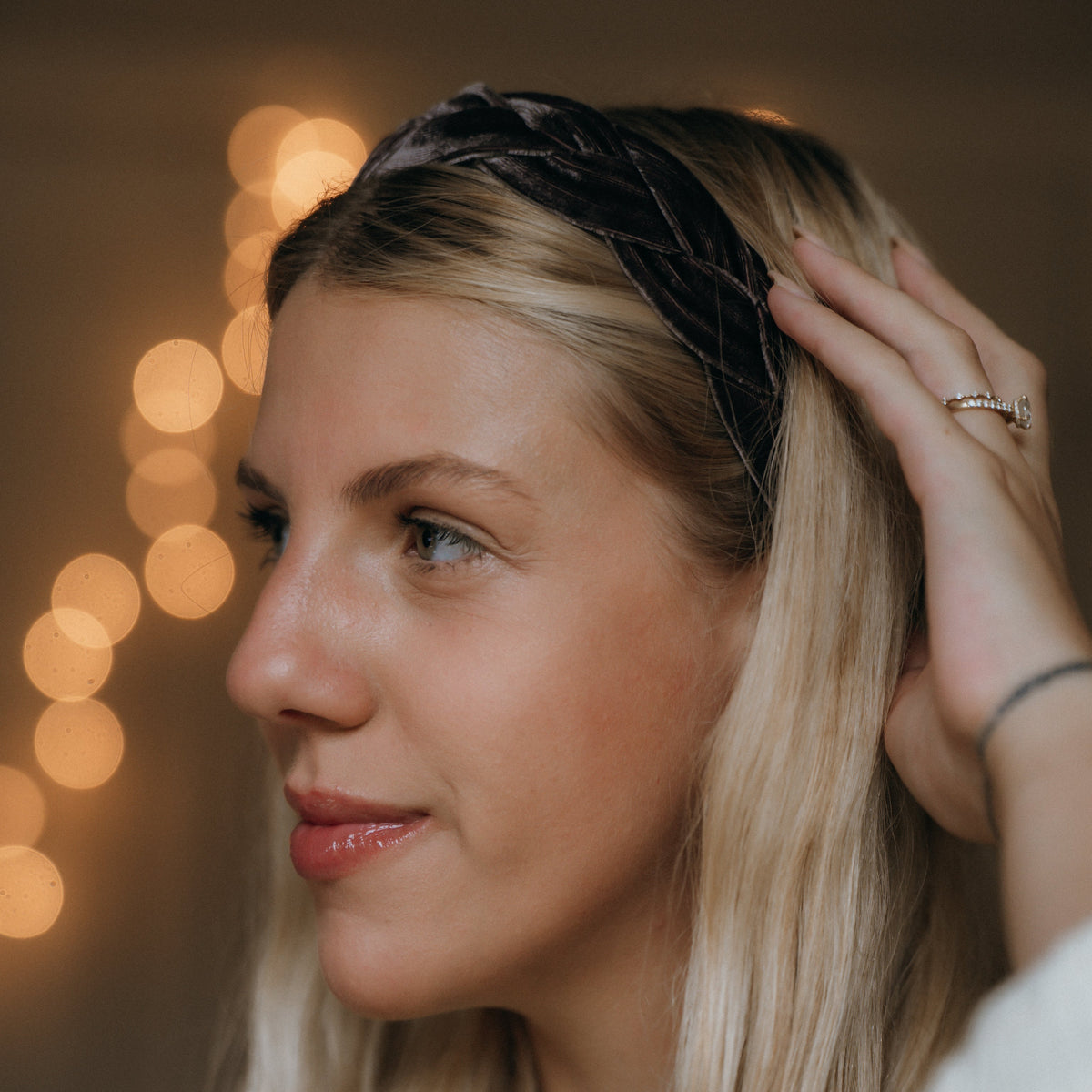 Woman wearing a velvet braided headband with blurred lights in the background