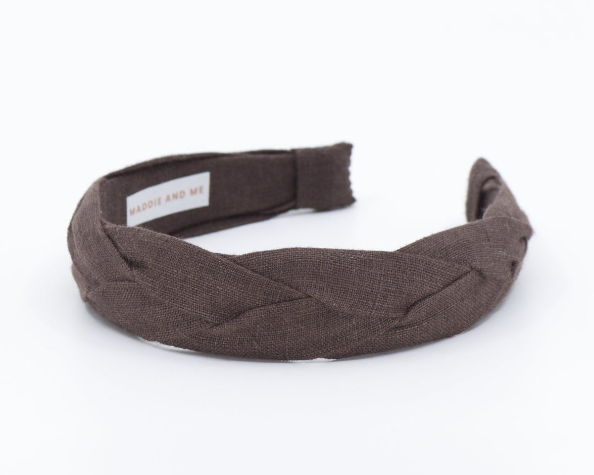 A dark brown braided fabric headband with a small white label reading 'MADDIE AND ME' on a clean white background.