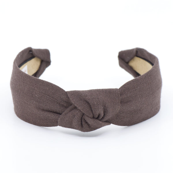 A fabric headband with a twisted knot in the center, shown on a plain white background. The headband is a dark brown color, and the inner lining is a light beige.