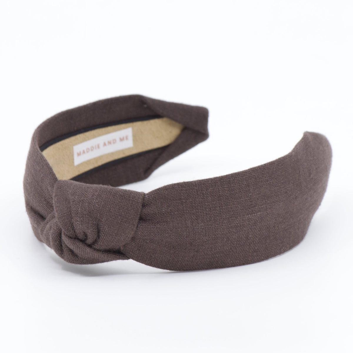 A dark brown fabric twist-front headband with a small white brand label inside, displayed on a clean white background.