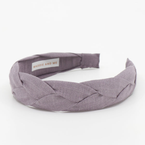 A wide braided fabric headband in a muted dusty purple color, featuring a small interior label that reads 'MADDIE AND ME'. The headband is photographed on a seamless white background.