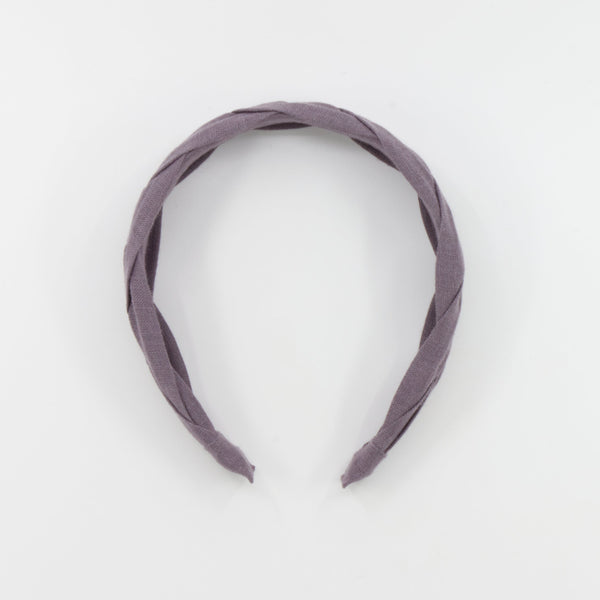 A braided fabric headband in a muted dusty purple color, photographed against a seamless white background.