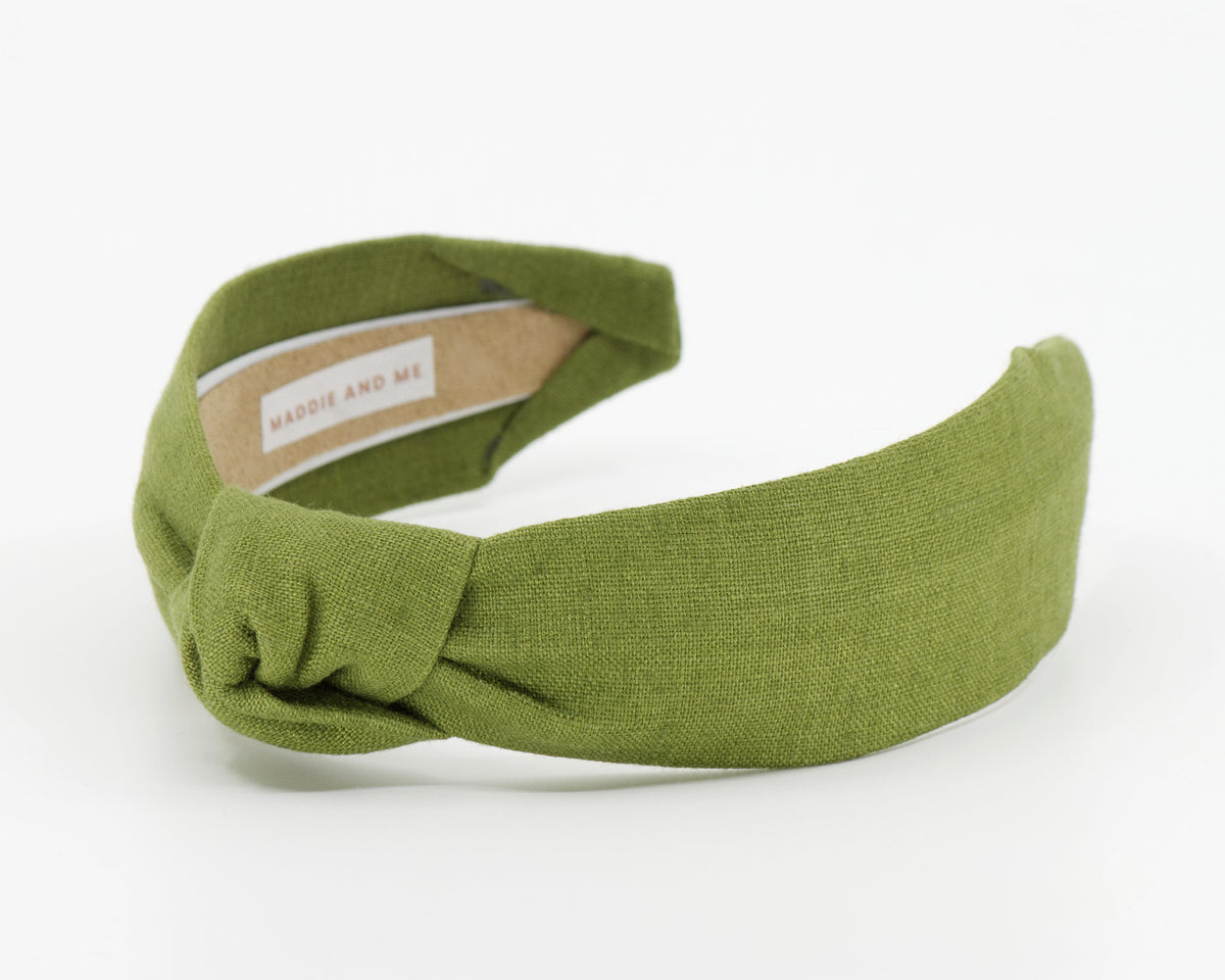 An olive green knotted fabric headband with a beige interior label reading 'MADDIE AND ME', photographed on a clean white background.
